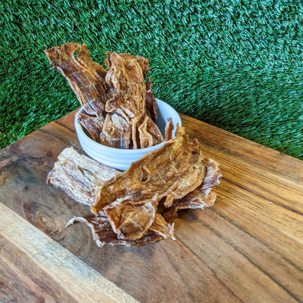Rabbit jerky in pinch bowl on wooden board with grass background Bonza Dog Treats