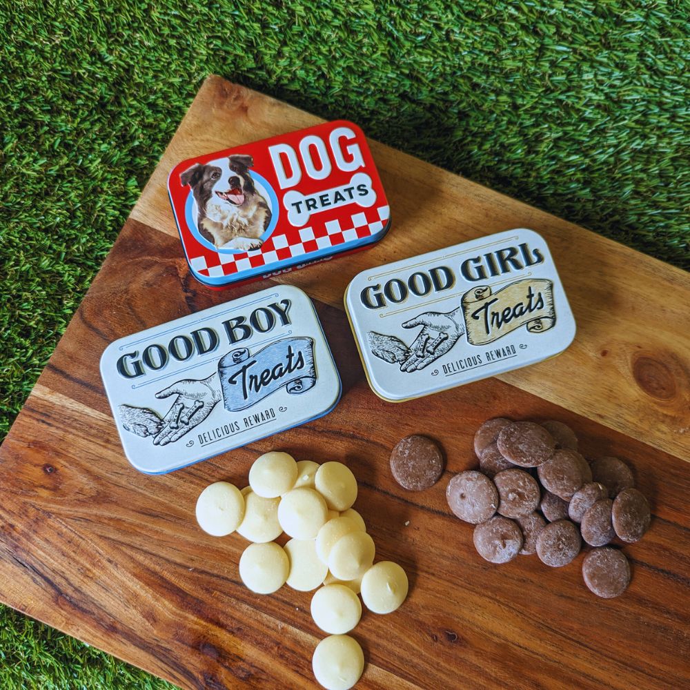 Three small dog treat tins displayed on a wooden board with yogurt drops and carob drops Bonza Dog Treats
