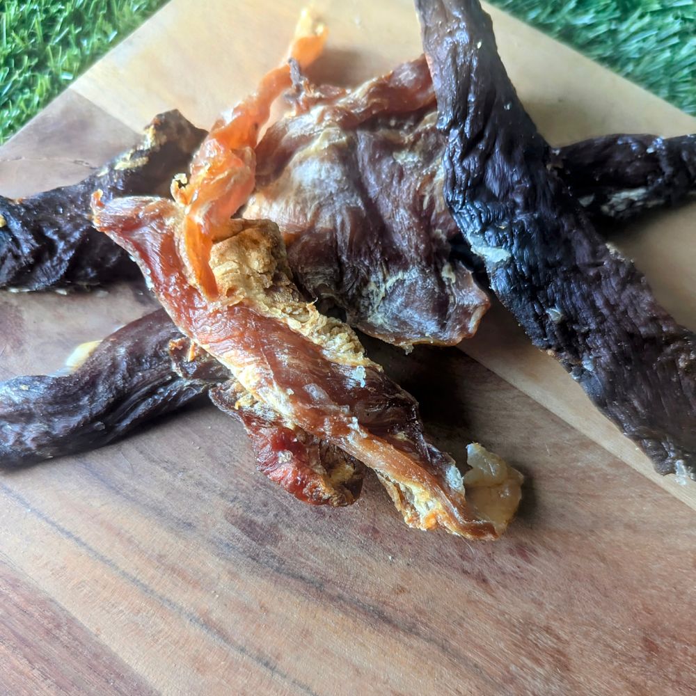 close up of crocodile jerky on a wooden cutting board with grass in the background
